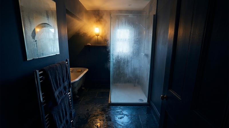 Steamy dark bathroom at night with a fogged glass shower and warm amber light, illustrating a hot shower before bed
